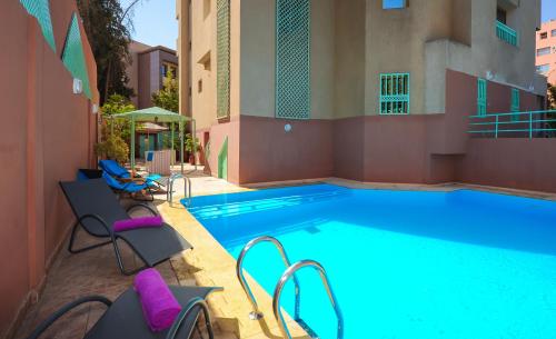 马拉喀什Appart-Hotel Amina Resort的一座大型游泳池,旁边是一座建筑,配有紫色椅子