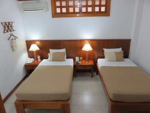 瓜亚基尔Hostal Macaw的配有两张桌子和两盏灯的房间的两张床