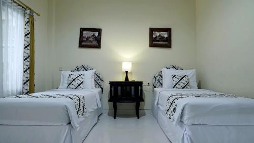 日惹Diana Hotel Jogja的一间卧室设有两张床和一张桌子上的台灯。