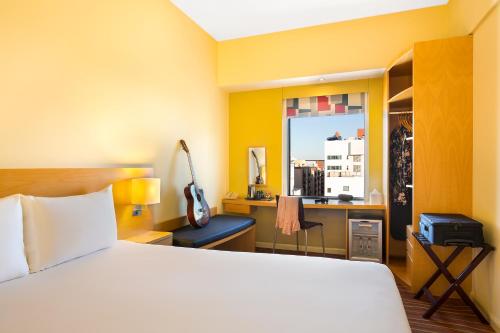 迪拜宜必思亚利加酒店的一间卧室配有一张床、一张书桌和一个窗户。