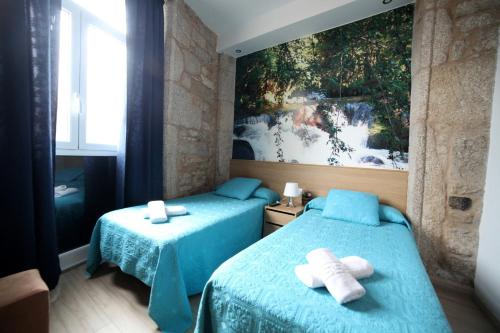 帕拉斯德丽Pension Pardellas的一间卧室配有两张带蓝色床单和绘画的床。