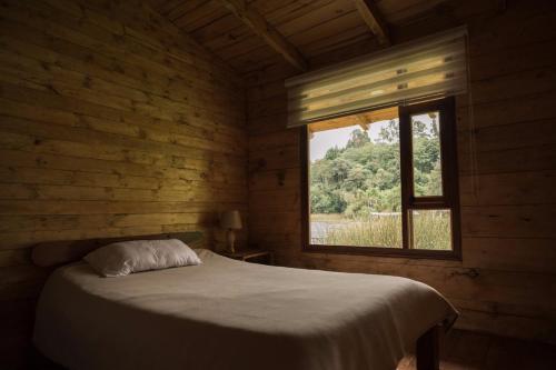 El EncanoHermosa Cabaña en La Cocha-Finca INDIANA的木制客房的一张床位,设有窗户