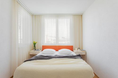 苏黎世Swiss Star Oerlikon Lodge - Self Check-In的一间卧室配有一张带橙色床头板的床和两个窗户。