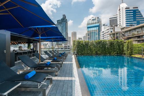 曼谷The Key Premier Hotel Sukhumvit Bangkok的大楼内带躺椅和遮阳伞的游泳池