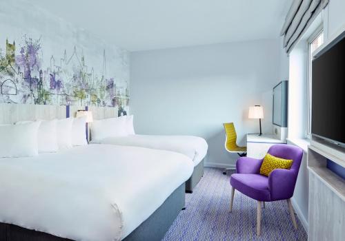 埃克塞特Leonardo Hotel Exeter的酒店客房设有一张大床和一张紫色椅子