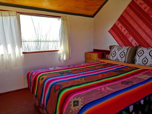 普诺Uros Titicaca Khantaniwa Lodge的一间卧室配有一张色彩缤纷的床和一扇窗户