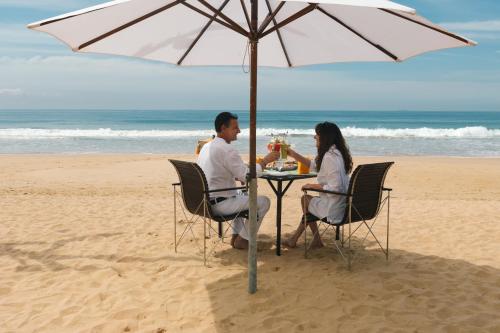 本托塔Amal Beach Hotel的两人坐在海滩上一把遮阳伞下的桌子上