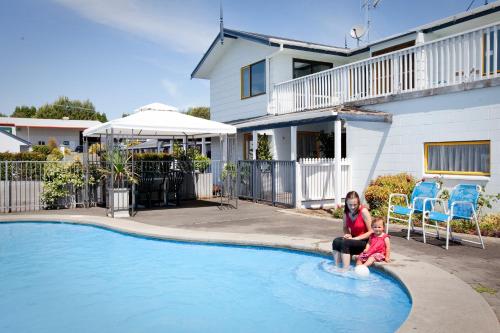 陶朗加Accommodation at Te Puna Motel的坐在游泳池边的女人和孩子