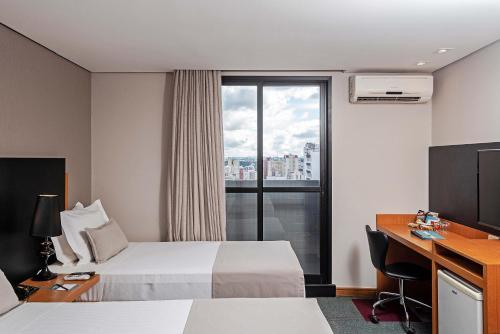 库里提巴Slaviero Curitiba Batel的配有一张床、一张书桌和一扇窗户的酒店客房