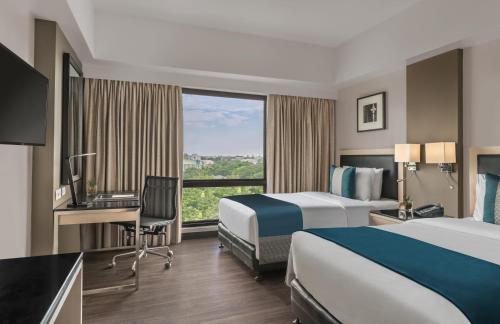 巴科洛德Seda Capitol Central Hotel的酒店客房设有两张床、一张书桌和一个窗户。