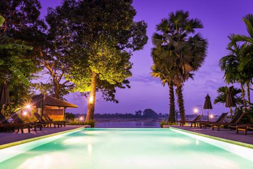 占巴塞河度假酒店的棕榈树和椅子的夜间游泳池