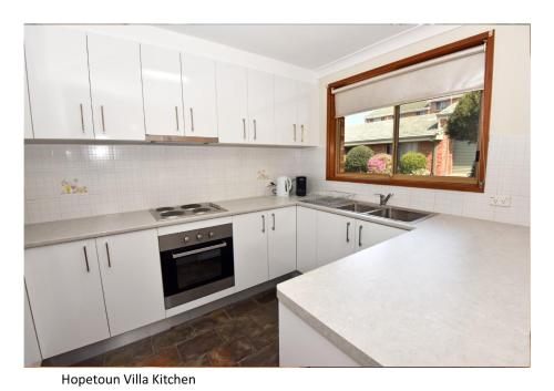 Woonona霍普顿别墅的厨房配有白色橱柜、水槽和窗户。