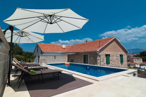 波斯蒂拉Apartments Ivana的一个带遮阳伞和椅子的游泳池以及一座房子