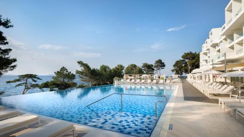 拉布Valamar Carolina Hotel & Villas的一个带白色椅子的游泳池以及大海