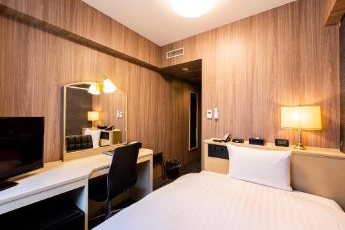 旭川Hotel Wing International Asahikawa Ekimae的酒店客房带一张床、一张书桌和一面镜子