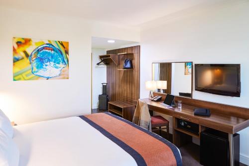 圣海伦斯Mercure St Helens的酒店客房设有一张床、一张书桌和一台电视机。