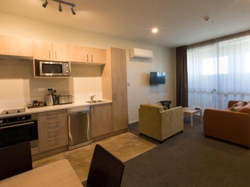 基督城Ramada Suites by Wyndham Christchurch City的厨房以及带沙发和桌子的客厅。