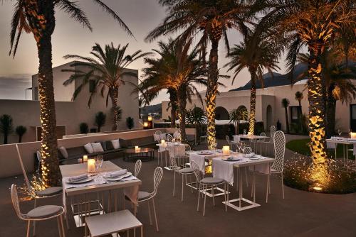 潘泰莱里亚Sikelia Luxury Hotel的餐厅拥有白色的桌椅和棕榈树