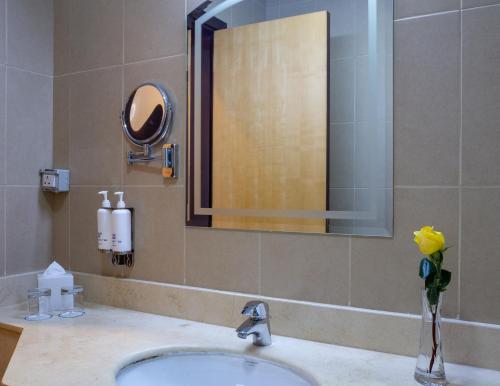 多哈Kingsgate Hotel Doha by Millennium Hotels的浴室水槽,配有镜子和花瓶