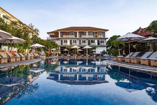 库塔Kuta Beach Club Hotel的酒店设有带椅子和遮阳伞的游泳池