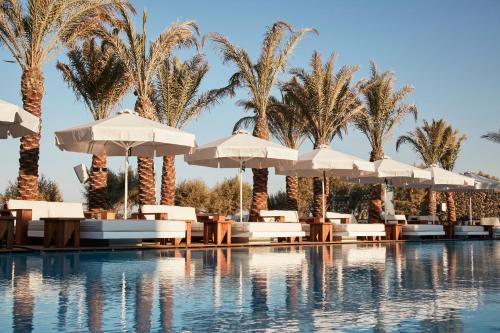 卡马利Nikki Beach Resort & Spa Santorini的一个带椅子和遮阳伞的游泳池以及棕榈树