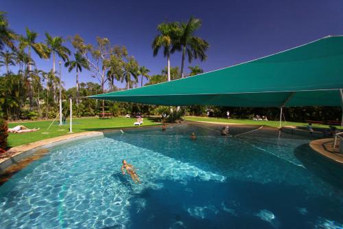 贾比鲁Aurora Kakadu Lodge的在带绿伞的游泳池游泳的人