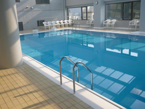 鸣门市鸣门海月酒店的一座带蓝色水和白色椅子的大型游泳池