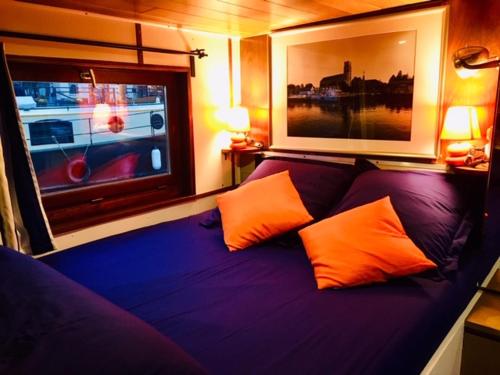 WambrechiesLa bigoudène的一张紫色的床,窗户旁配有两个橙色枕头