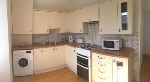 阿德罗森Arran Ferry Apartment的厨房配有白色橱柜、炉灶和微波炉。