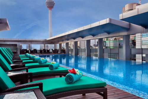 吉隆坡吉隆坡宾乐雅服务公寓的酒店游泳池设有绿色椅子,酒店大楼