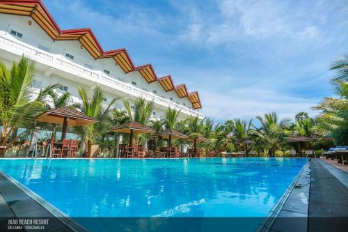 亭可马里JKAB Beach Resort的大楼前带椅子和遮阳伞的大型游泳池