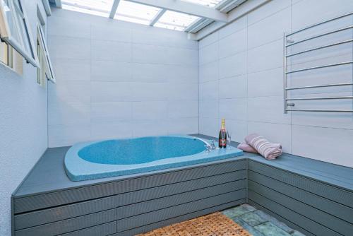 罗托鲁瓦Silver Fern Rotorua Suites & Spa的浴室设有蓝色浴缸,提供一瓶葡萄酒