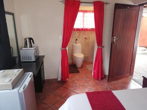 Sasolburg52 Oaks Guest House的一间带红色窗帘的卧室和一间带卫生间的浴室