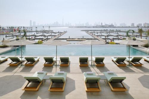 迪拜云溪港葳达酒店的一组椅子和遮阳伞,位于游泳池旁