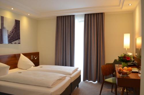慕尼黑阿古斯特恩穆尼辰酒店的酒店客房设有两张床、一张桌子和一张桌子。