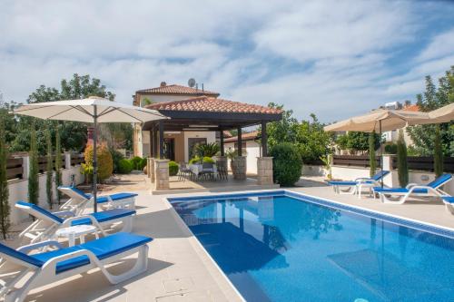 帕福斯Kallizoni villa的房屋旁的游泳池配有椅子和遮阳伞