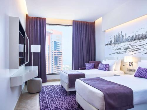 迪拜Mercure Dubai Barsha Heights Hotel Suites And Apartments的酒店客房设有两张床和大窗户。