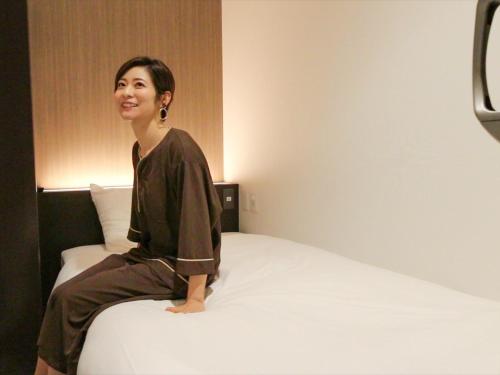 船桥市LEO YU Capsule Hotel Nishifunabashi的坐在床上的女人