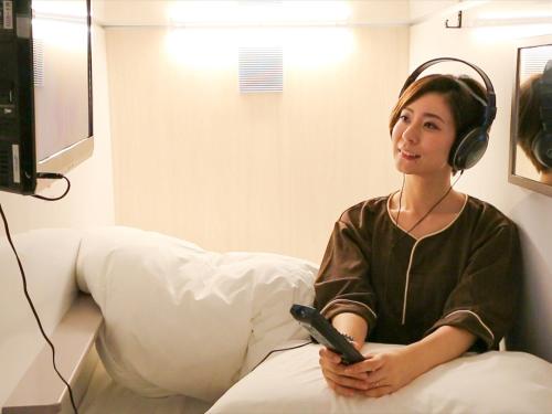 船桥市Leo Yu Capsule Hotel Funabashi的戴耳机并带遥控器的女人