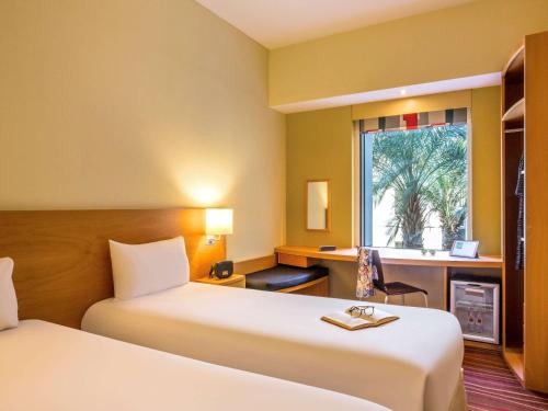 迪拜ibis Mall Avenue Dubai的酒店客房设有两张床、一张书桌和一个窗户。
