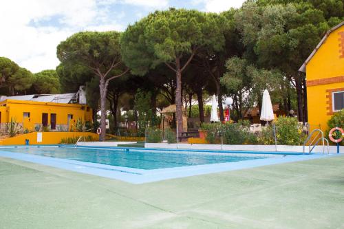 贝赫尔-德拉弗龙特拉维赫尔露营酒店的一座游泳池,旁边是一座黄色的房屋和树木