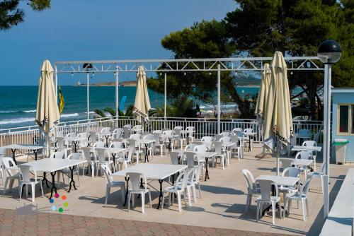 维耶斯泰Villaggio Capo Vieste的一组桌子、白色椅子和遮阳伞