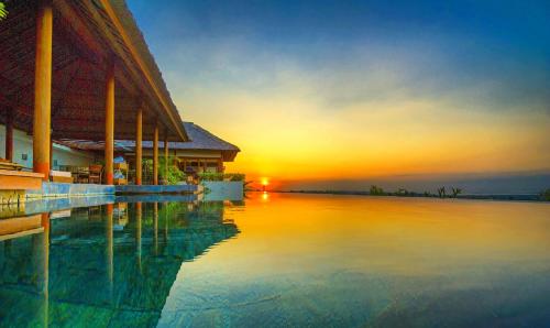 金巴兰巴厘岛金巴兰长屋旅馆的建筑物旁水面上的日落