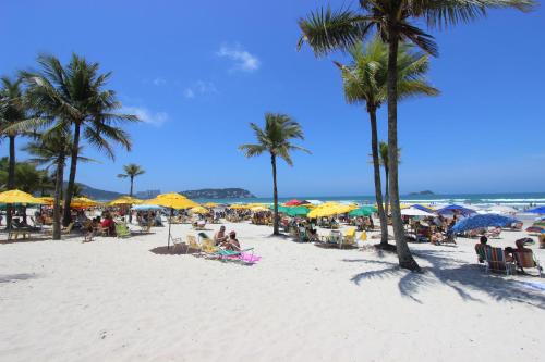 瓜鲁雅Hotel Ilhas do Caribe - Na melhor região da Praia da Enseada的一群人坐在海滩上,拿着遮阳伞