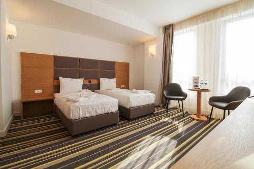 BuzăuHotel Avenue - Avenue Hotels的酒店客房带两张床和一张桌子以及椅子。