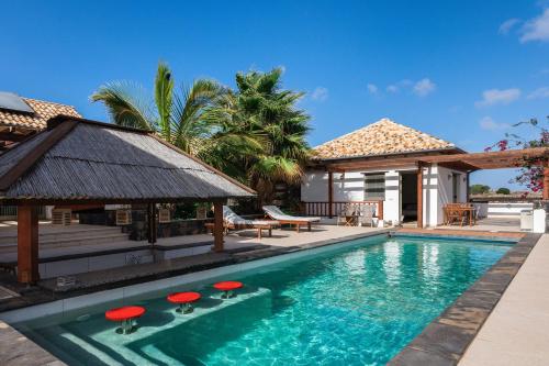 拉哈雷斯Villa Annunaki的一座房子旁的游泳池,游泳池旁设有红色凳子