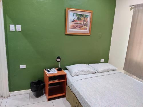 西班牙港Woodbrook on the Avenue的一间卧室设有绿墙、一张床和一个床头柜