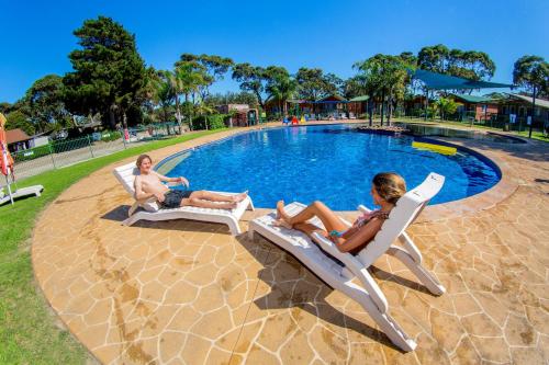 莫鲁亚大4莫卢亚海德东海豚海滩度假公园的两人坐在游泳池旁的草坪椅上