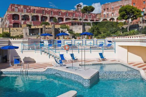 那不勒斯皇家大陆酒店的大楼前的游泳池配有椅子和遮阳伞