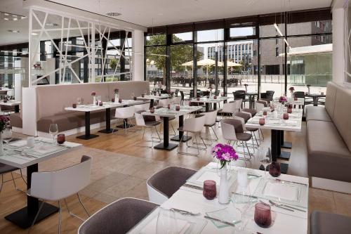 沃尔夫斯堡INNSiDE by Meliá Wolfsburg的餐厅设有白色的桌椅和窗户。